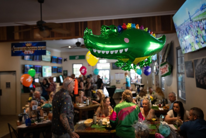 A crocodile balloon floating in a busy tavern with crowds in the background