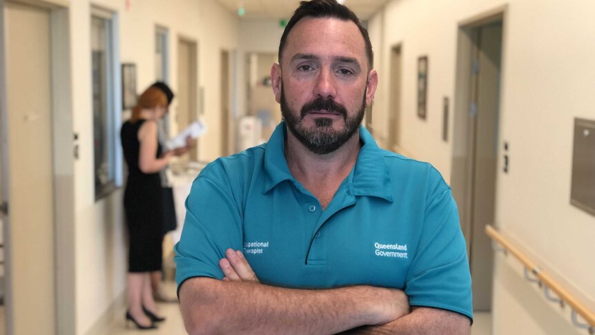 Occupational therapist Russell Plumbridge-Jones stands in a corridor at Robina Hospital with his arms folded.