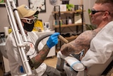A person removing tattoos from a man's arm, both wearing protective glasses and sitting