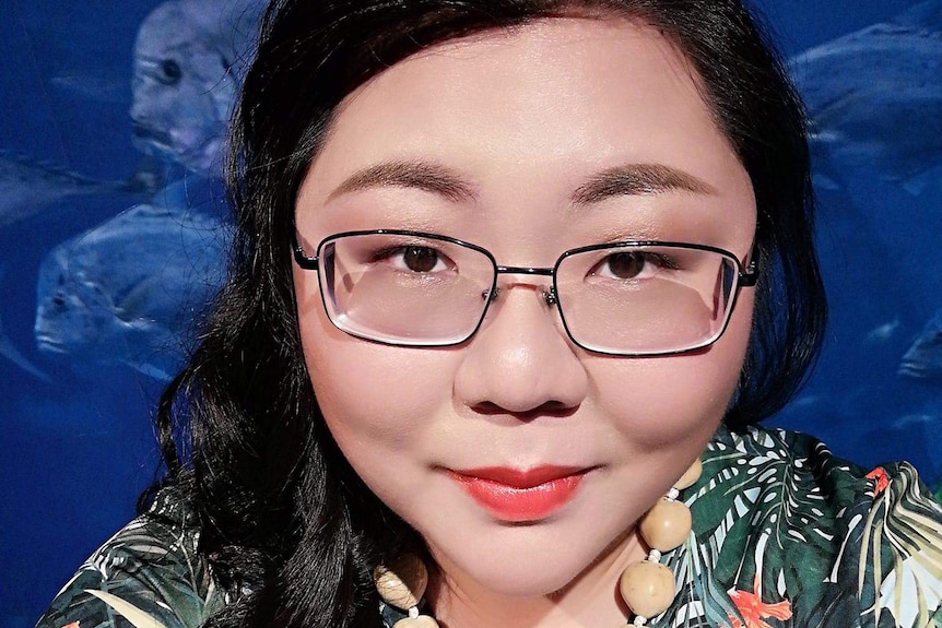 A woman with black hair and glasses taking a selfie in front of a fish tank.