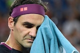 Roger Federer looks tired as he uses a towel to wipe sweat from his brow.