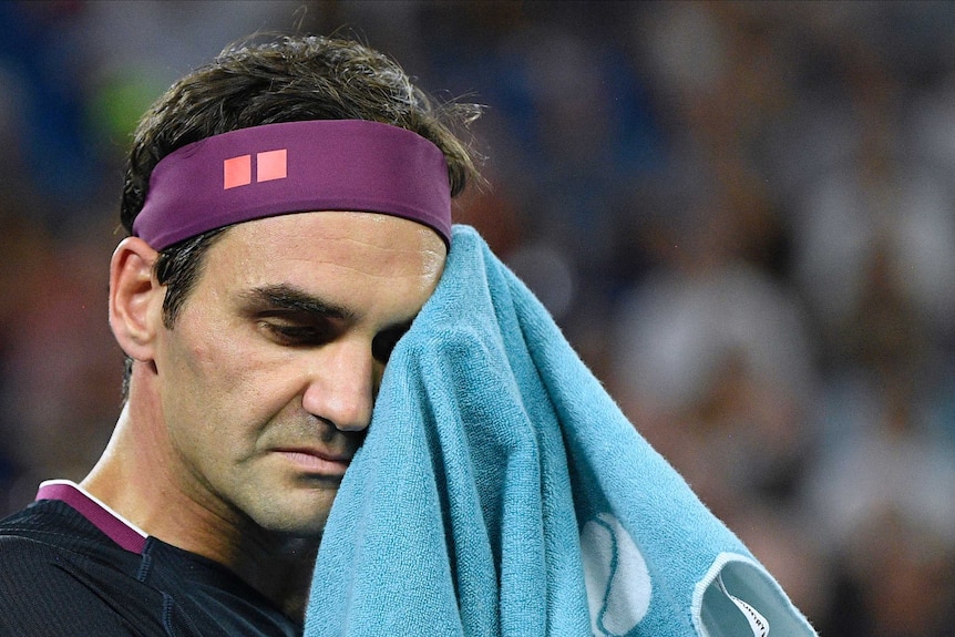 Roger Federer looks tired as he uses a towel to wipe sweat from his brow.