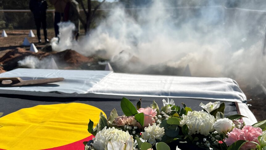 People watch on as smoke billows over a coffin draped in an Aboriginal flag.
