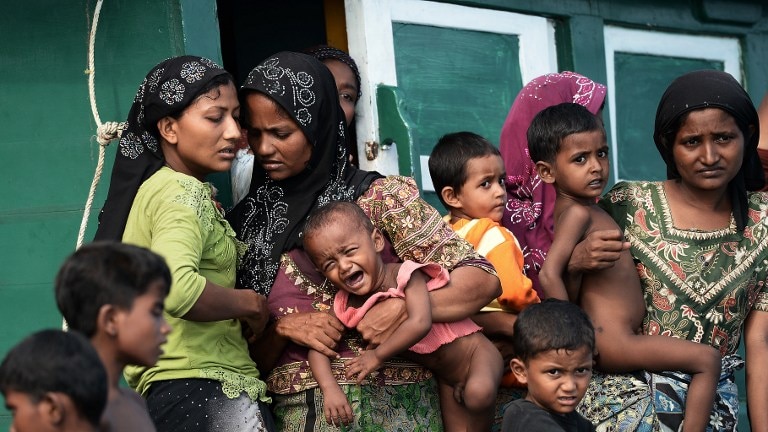 Rohingya migrant women holding children as they stand on a boat drifting in Thai waters.