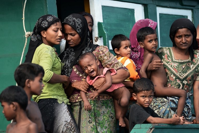 Rohingya migrant women holding children as they stand on a boat drifting in Thai waters.