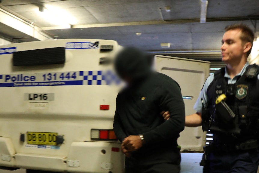 Man in handcuffs being led from NSW police van. 