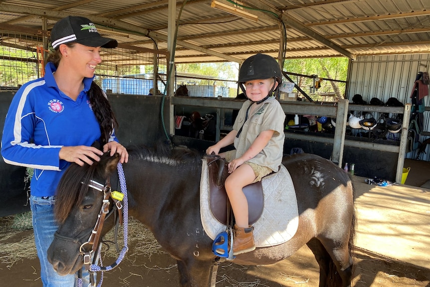 woman stands next to young boy sitting on a pony