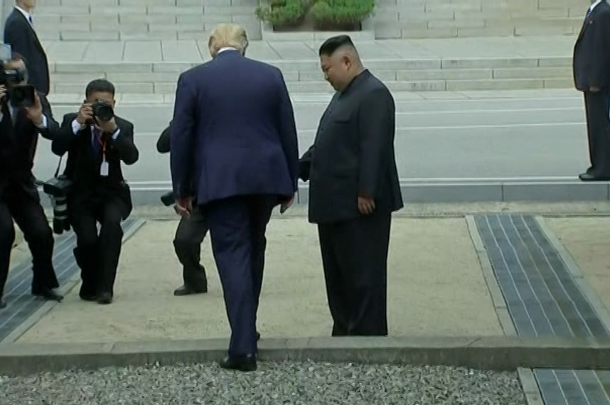 Donald Trump, left, prepares to cross the border as Kim Jong-un stands to his right with photographers seen in distance.
