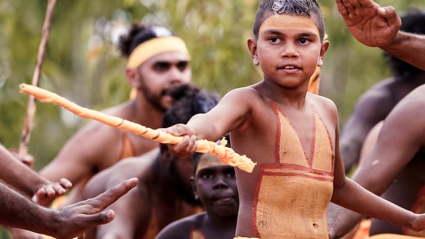 A young Indigenous boy in traditional body paint participates in a dance at Garma Festival