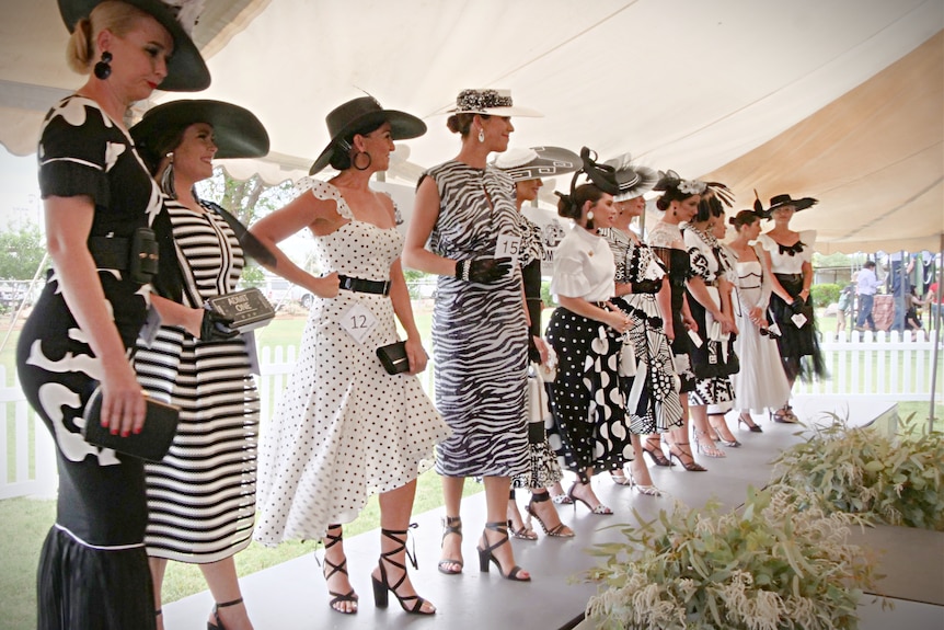 A row of ladies dressed in black and white Derby Day fashion stand on-stage