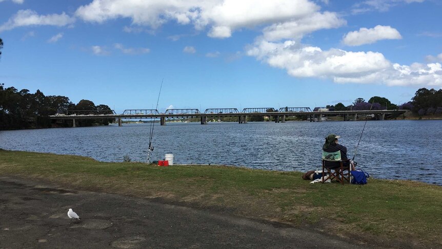 A recreational fisher sits on a chair at the shore of the Shoalhaven River at Nowra.