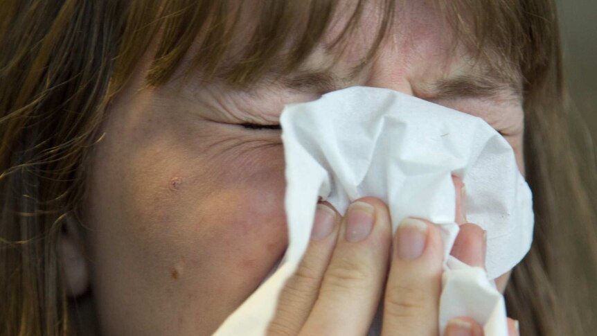 A woman scrunches her eyes and puts a tissue over her face.