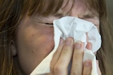 A woman scrunches her eyes and puts a tissue over her face.