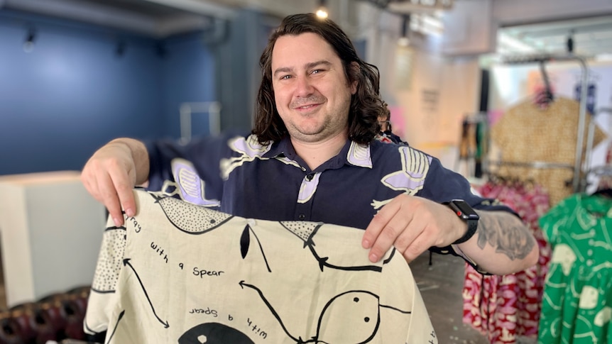 Magpie Goose owner Troy Casey holds up a shirt with a sting ray pattern on it.