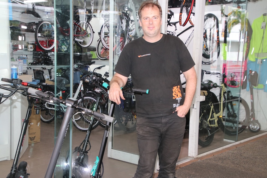 Anthony Van Duyn from Cairns Electric Bikes standing out front of his shop with several scooters