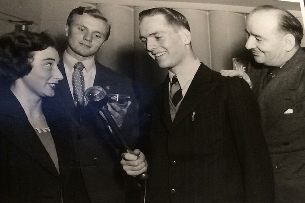 Black and white photograph of a young woman and two young men, one of whom is john pickup, holding a microphone and smiling