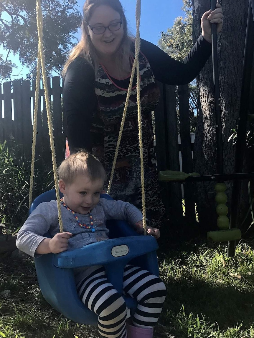 Mother pushing her three year old son on a backyard swing.