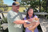 A man in a baseball cap pats a cat being held  by a woman with brown hair
