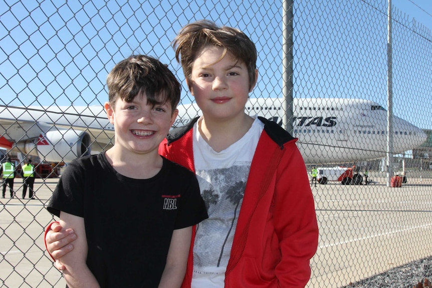 Two boys in front of a wire fence at an airport.