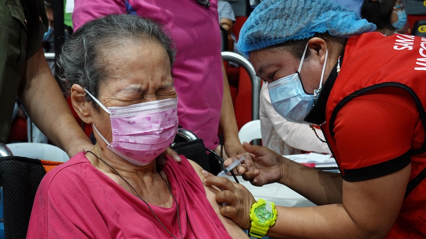 An elderly Fillipino woman shuts her eyes as she recieves a vaccine