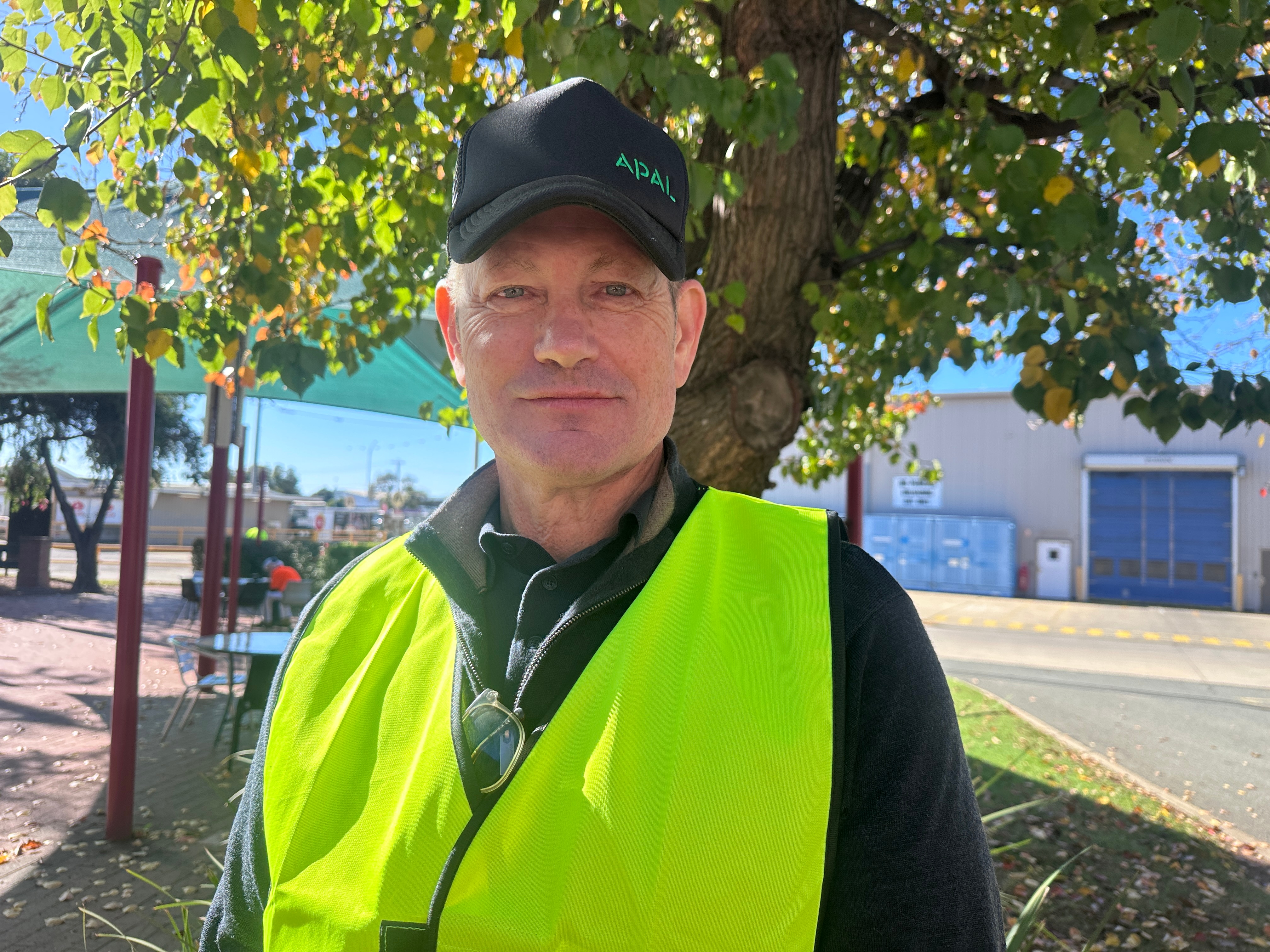 A man in a cap and high visibility vest stands in a factory courtyard