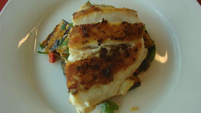 Barbecued fish, resting on grilled pumpkin, on a white plate.