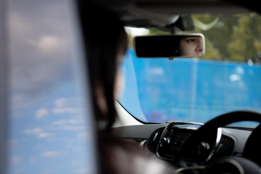 A woman's reflection in the rear view mirror of a car while driving.