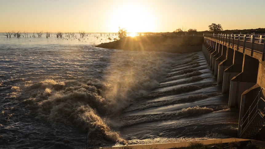 water flowing through a weir into a wide expanse as the sun sets behind, golden late afternoon light