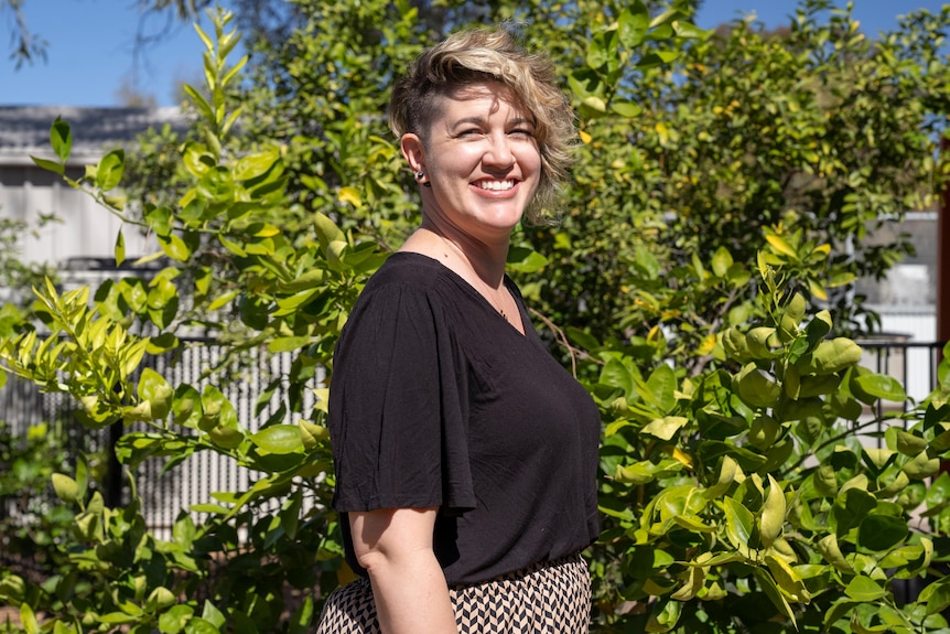 Woman with short hair wearing black t-shirt in front of green tree