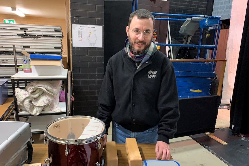 Border Music Camp Director Alastair McKean stands behind  drums on a table in a music storage room.