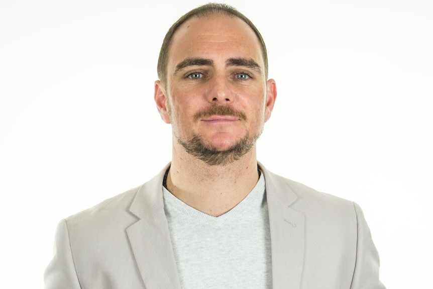 man with brown facial hair wearing grey blazer smiling at camera