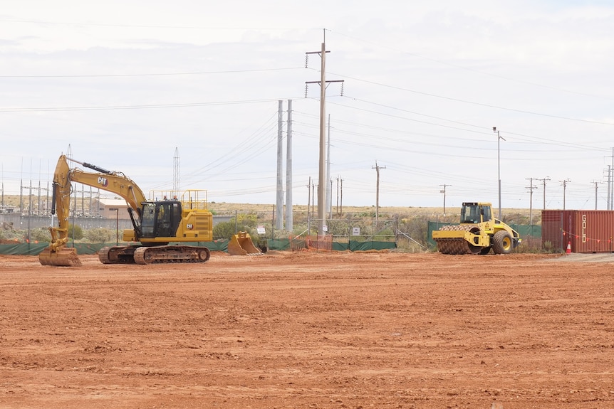 Two construction vehicles sitting idle in a patch of dirt with poles and metal boxes around them