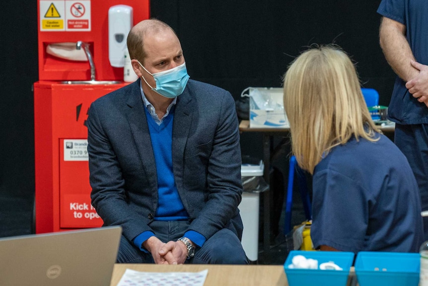 Prince William wearing mask, seated, speaks to health workers
