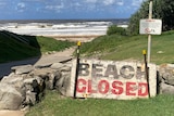 A sign reading 'beach closed' is placed next to a pathway that leads to a beach.