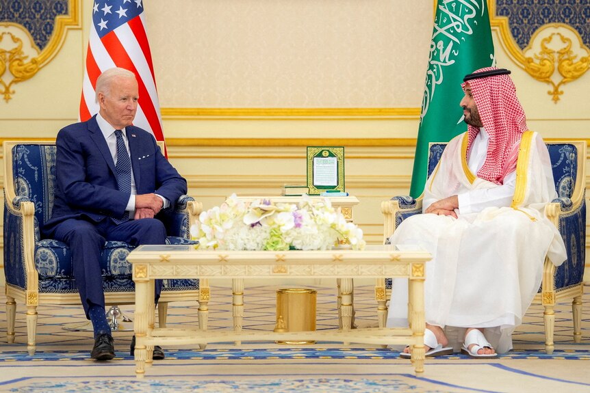 Joe Biden sits across from Crown Prince Mohammed bin Salman in a yellow room. Their respective flags are behind them. 