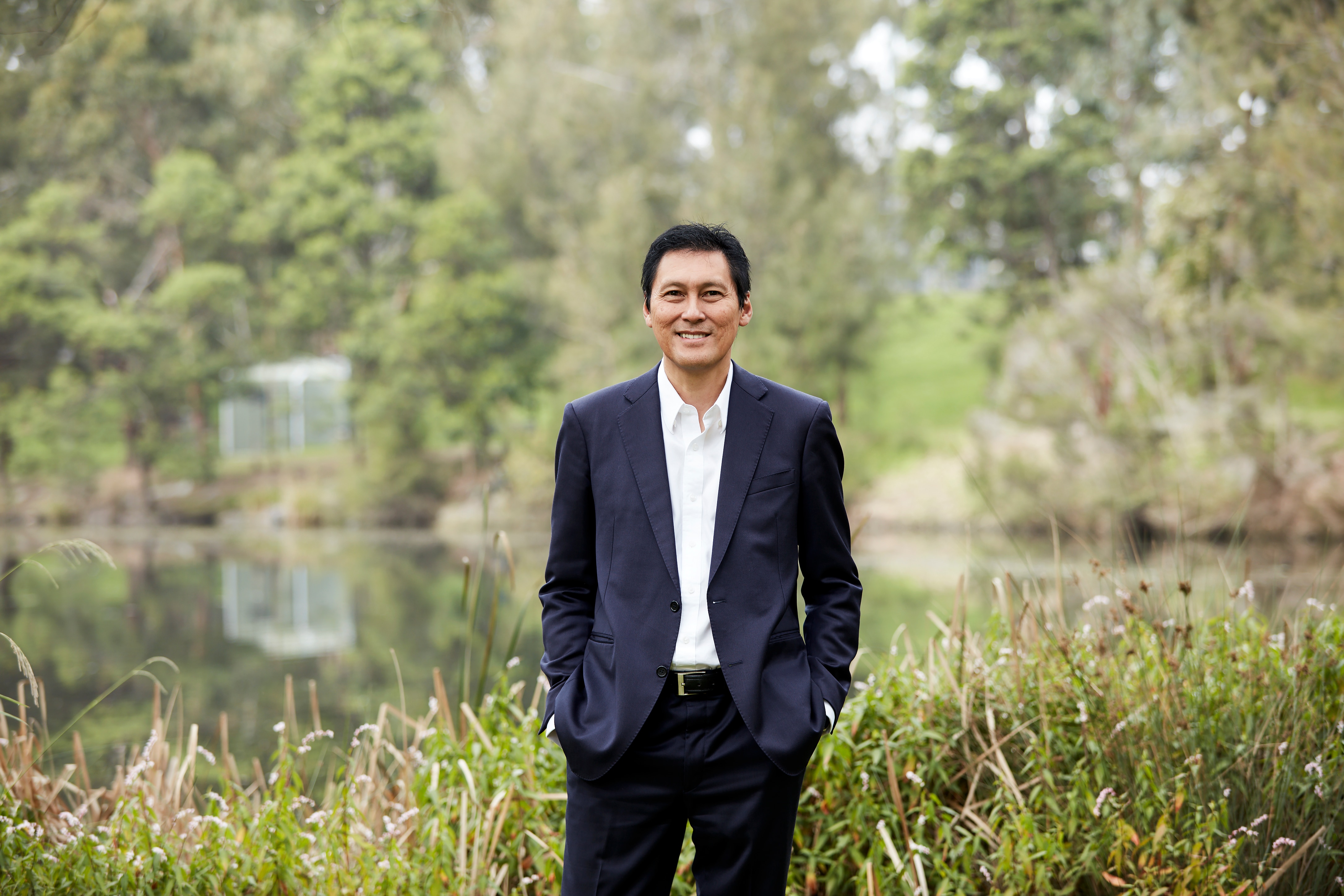 Um homem de terno fica em frente a um corpo de água na natureza.