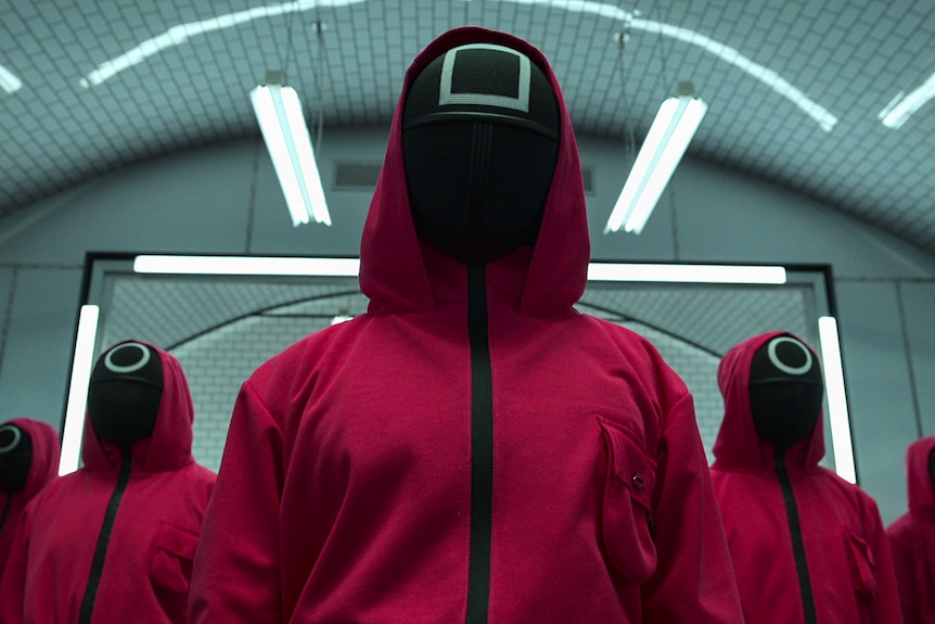 People lined up behind each other dressed in a red suit and black and white mask
