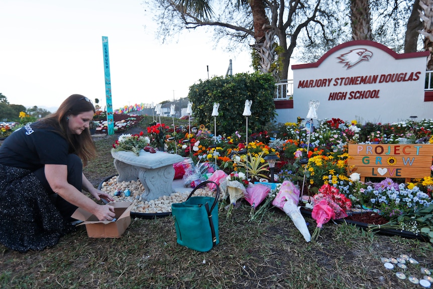 A woman bends down to lay flowers in front of a tribute at a sign that reads Marjory Stoneman Douglas High School. 