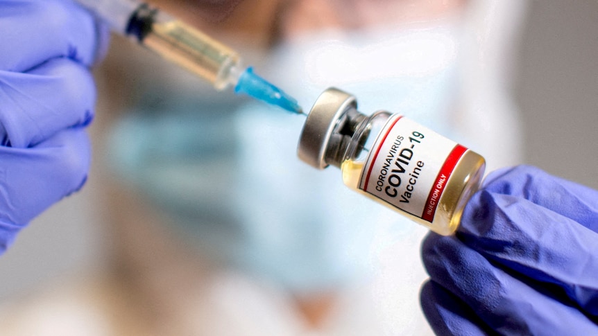A woman holds a medical syringe and a small bottle labelled "Coronavirus COVID-19 vaccine" 