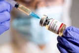A woman holds a medical syringe and a small bottle labelled "Coronavirus COVID-19 vaccine" 