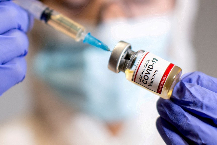 A woman holds a medical syringe and a small bottle labelled "Coronavirus COVID-19 vaccine" 