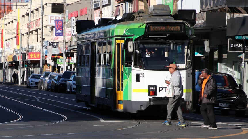 Two people walk across an intersection in front of a tram on a suburban street.