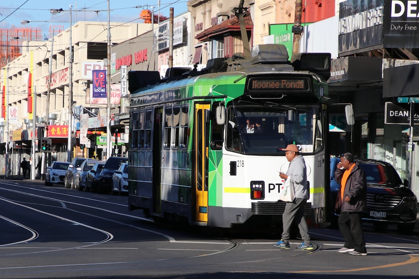 Two people walk across an intersection in front of a tram on a suburban street.