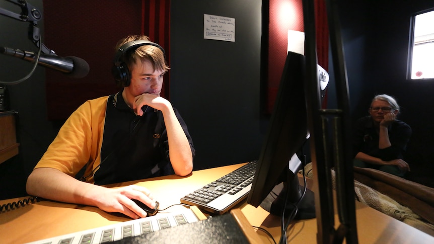 Ben sitting at a radio panel with his teacher Louise Olsen in the background.