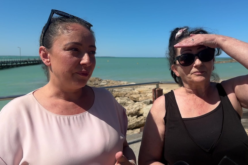 Two people stand along a beach front.