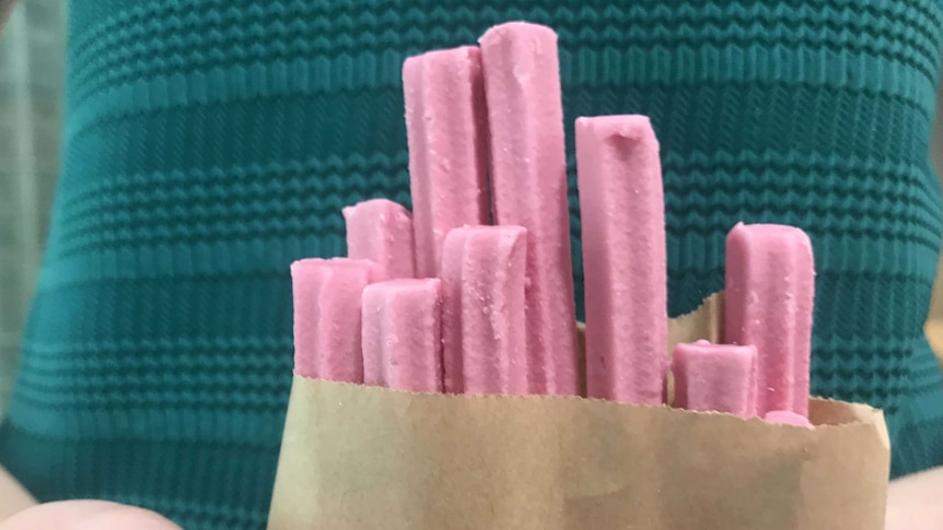 A woman in a green dress holding a brown bag filled with pink musk sticks