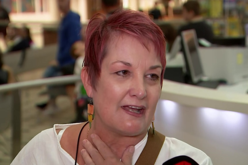 A middle-aged woman with short red hair speaks at an airport.