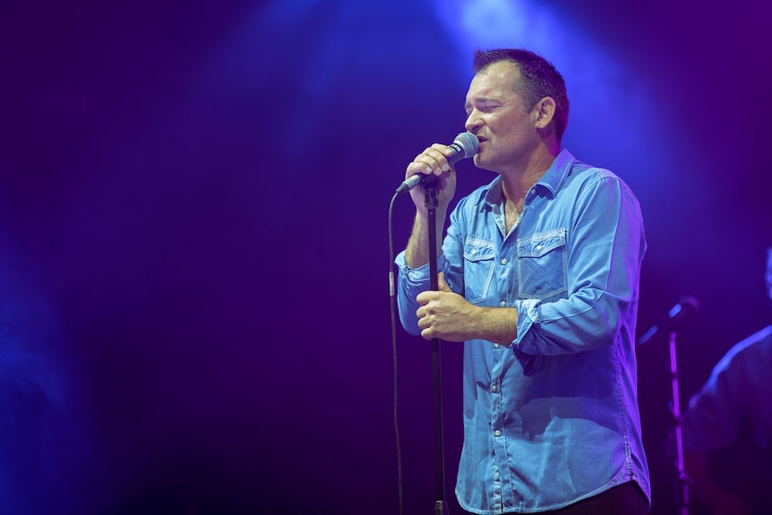 Country star Adam Brand singing soulfully on a concert stage.