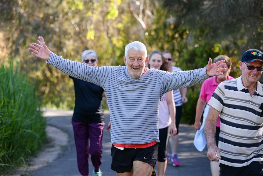 A man with outstretched arms walks parkrun.
