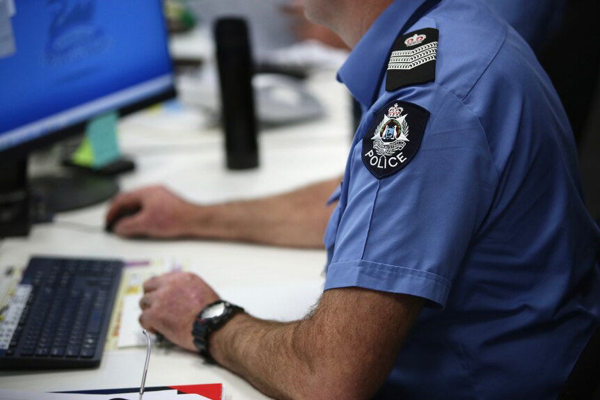 An unidentifiable WA Police senior sergeant sits at his desk using the computer.